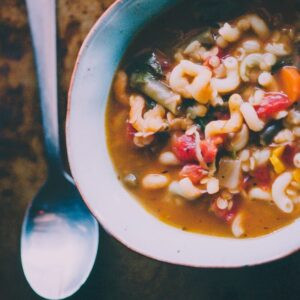 A bowl of gluten-free vegan lentil minestrone soup with visible lentils and vegetables in a tomato-based broth.