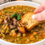 A photo showcasing a slice of baguette being dipped into a comforting bowl of split pea soup.