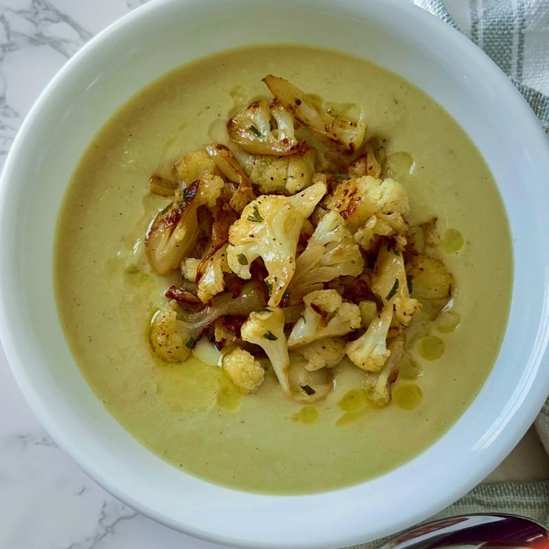 Creamy roasted cauliflower soup in a bowl with some roasted cauliflower florets garnished on top. 