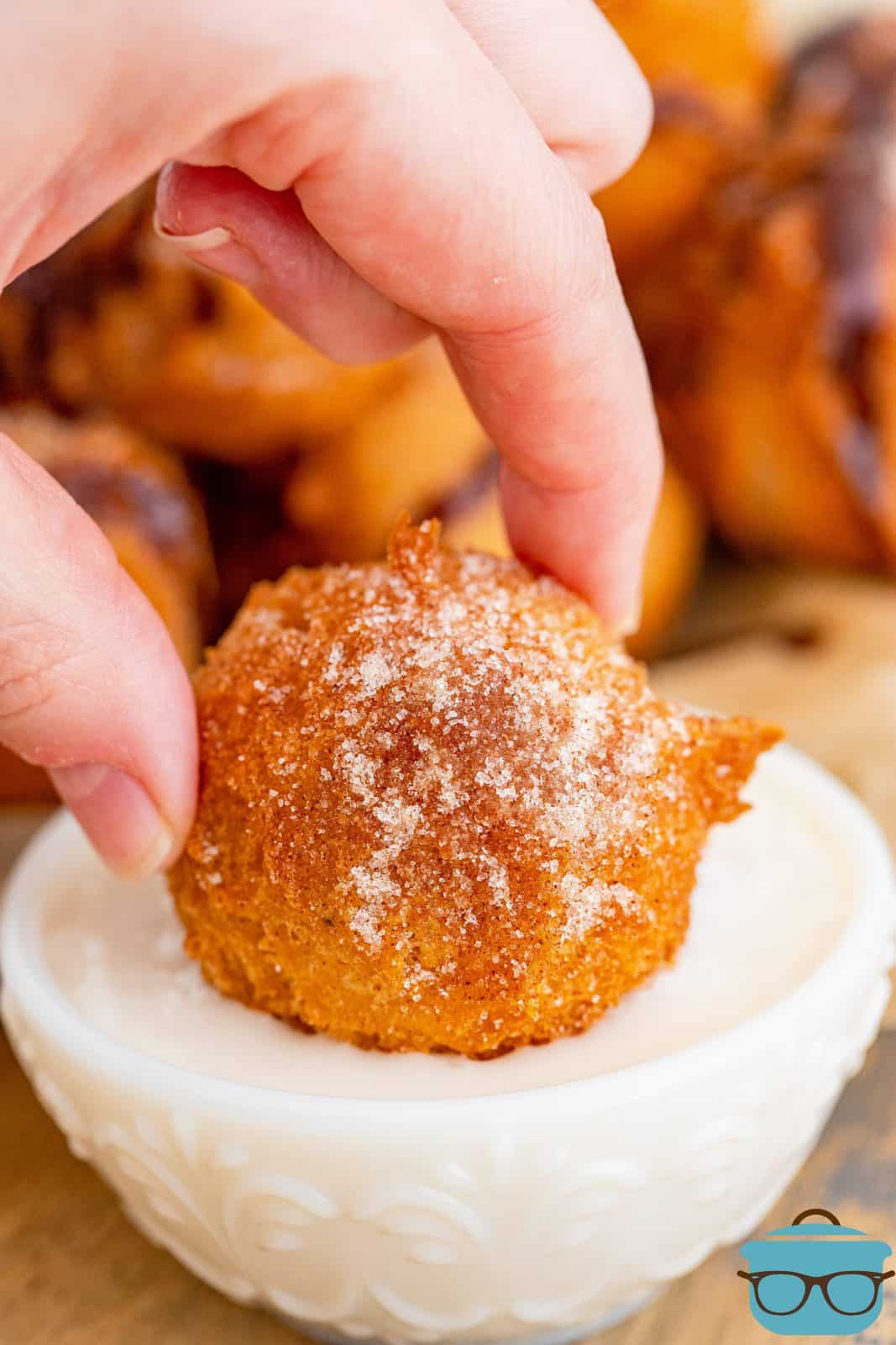 Pancake Puppies shown being dipped in vanilla icing in a bowl.