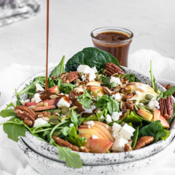 pouring balsamic dressing on a spinach salad